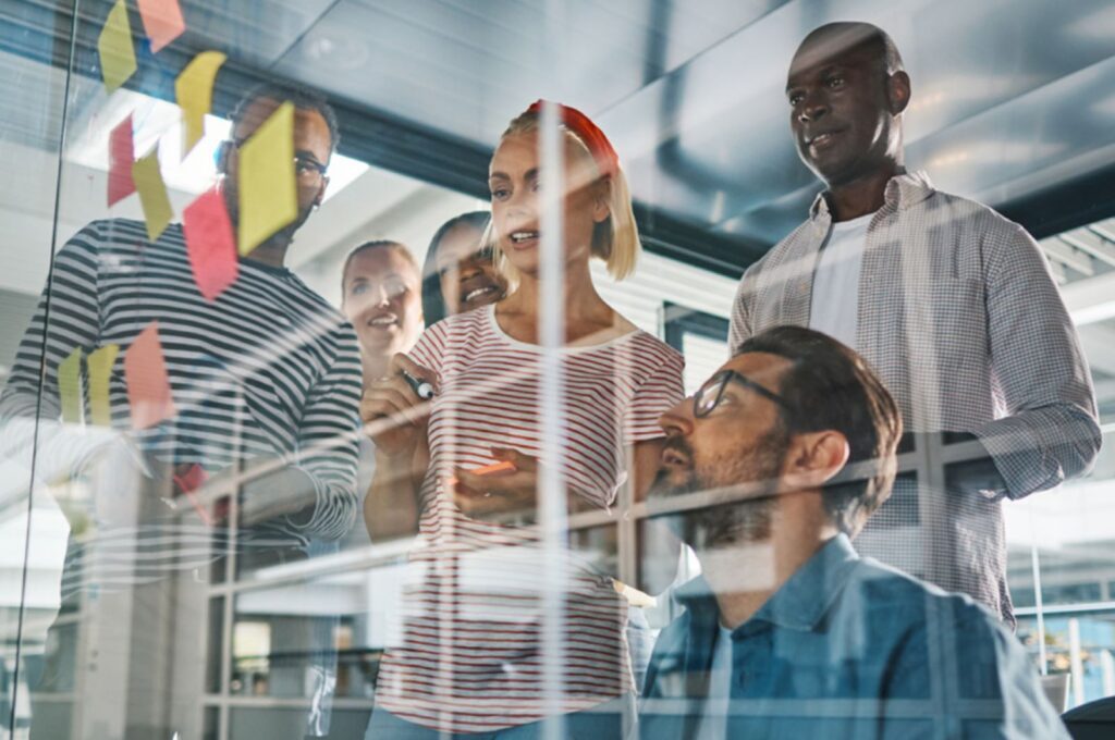 Équipe en atelier collaboratif devant une vitre avec des post-it pour illustrer la coopération dans les équipes.