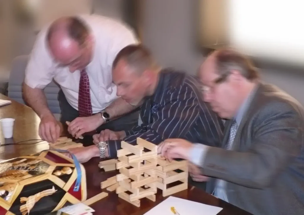 Trois participants réalisent une construction en bois pendant Le Défi des 5 Lagons, jeu Eikos sur la coopération entre équipes.